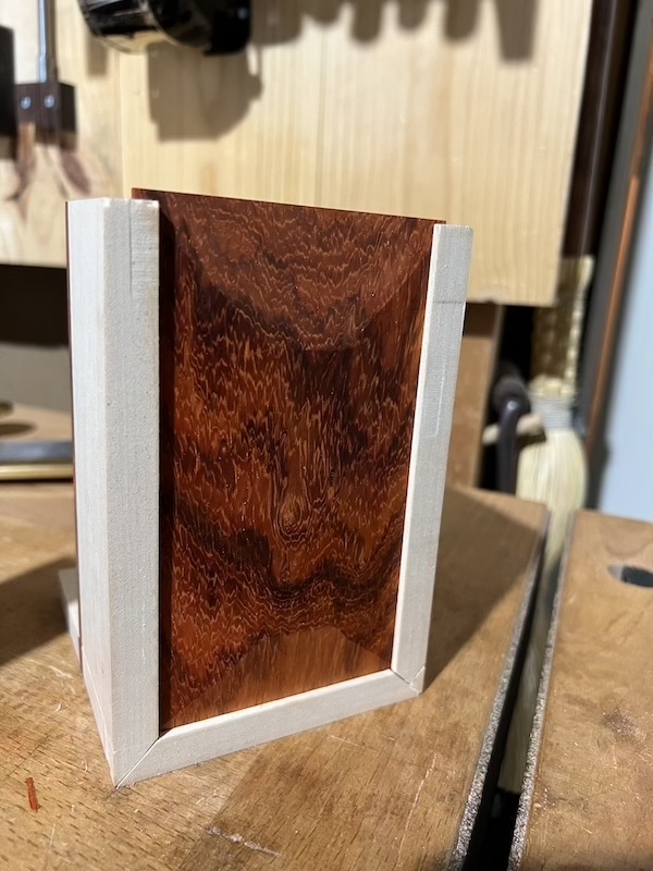 A picture of a box standing on one end with a padauk panel slid into the bottom groove.