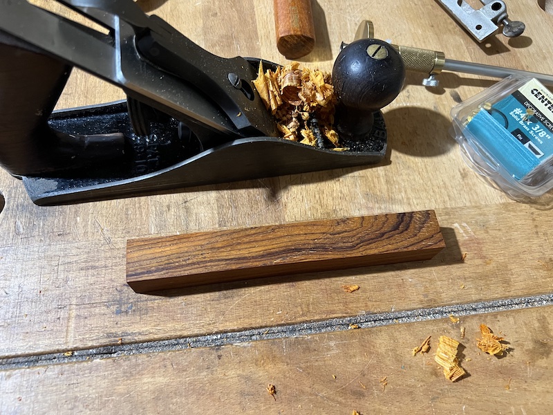 A number 4 handplane with shavings next to a cocobolo pen blank with wispy grain.