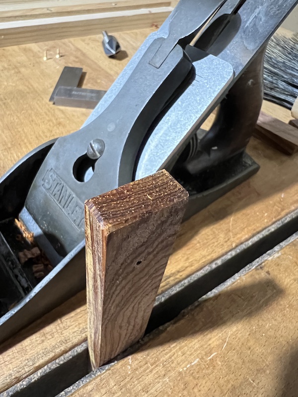 A Number 4 handplane next to a wooden fence mounted in a tail vise.