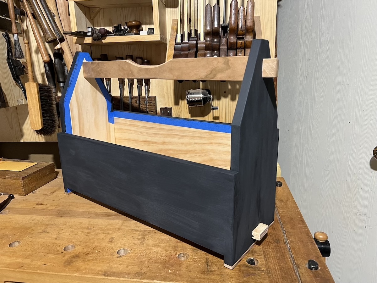 A tool tote with the outside painted in black milk paint, and blue painters tape masking the inside.