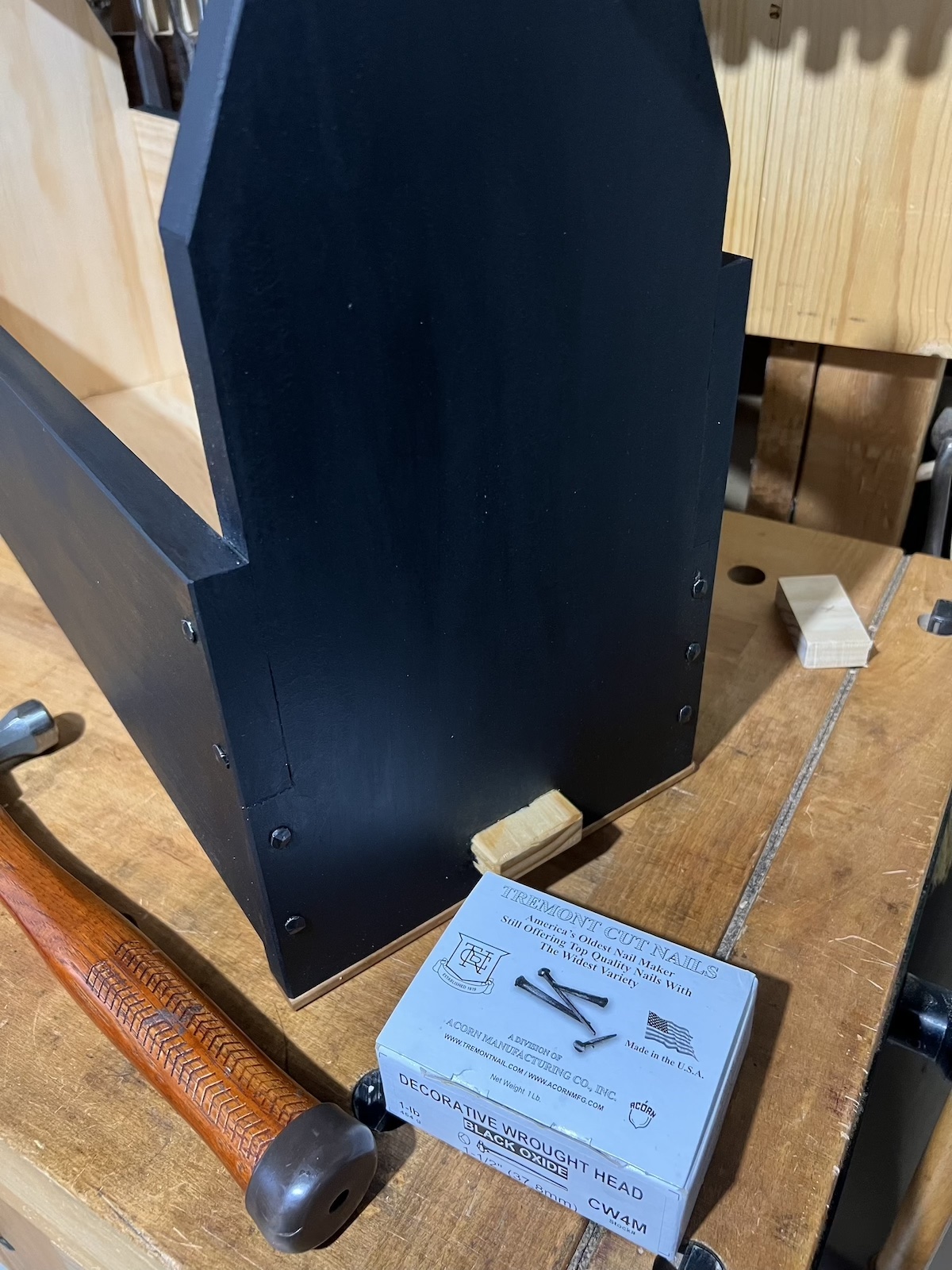 The end view of the tool tote showing nails reinforcing the half-lap joinery.  A hammer and box of decorative wrought head nails is next to the box.